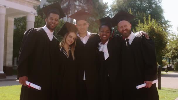 Σε μια τέλεια ηλιόλουστη μέρα μετά την αποφοίτηση ομάδα πολυφυλετικών φοιτητών απόφοιτοι ποζάρουν όλοι μαζί μπροστά από την κάμερα στον κήπο του κολεγίου — Αρχείο Βίντεο