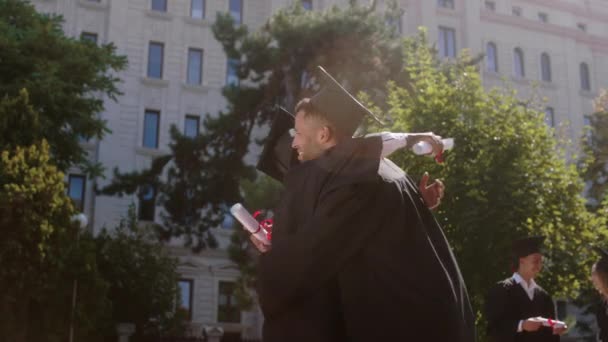 Junge gut aussehende schwarze Dame und ihr Kollege schwarzer Mann nach dem Abschluss umarmen einander sehr aufgeregt und diskutieren, während sie Diplome halten — Stockvideo