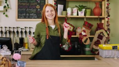 Kahve dükkanında kameranın önünde gülümseyen ve poz veren güzel bir bayan. Tablet çekiminde küçük işletme kavramının önünde duruyor.