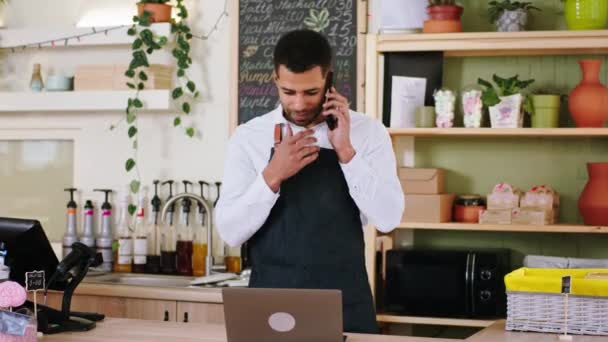 Guapo barista hombre afroamericano utilizando el portátil para escribir un poco de orden del cliente en el acogedor concepto de cafetería de la pequeña empresa y empresario — Vídeo de stock