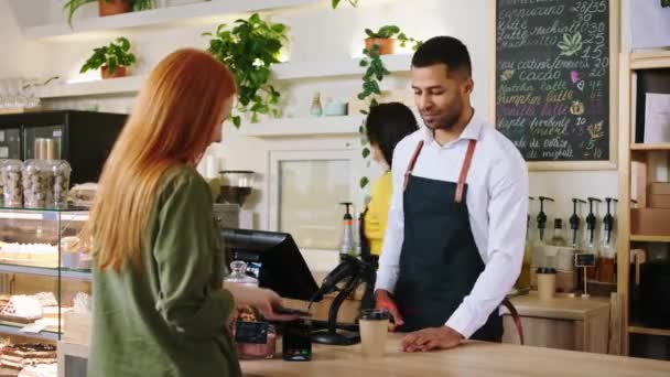 In de coffeeshop bar goed uitziende Afro-Amerikaanse man barista op de terminal de verkoop van koffie aan de klant erg blij en opgewonden — Stockvideo