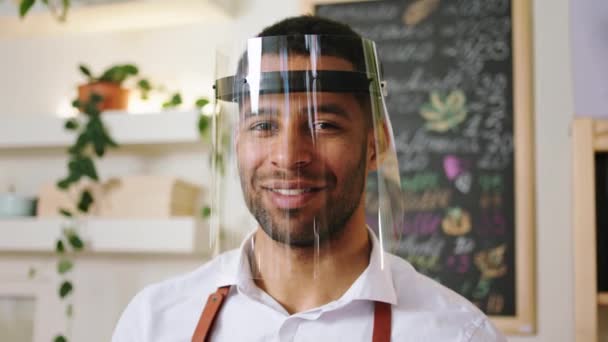 Closeup to the camera portrait of a barista man Afro American with protective mask posing to the camera smiling large — Stock Video