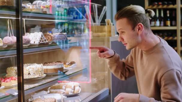 在面包店的咖啡店里，迷人而英俊的顾客从橱窗冰箱里挑选一些甜点，他很兴奋 — 图库视频影像