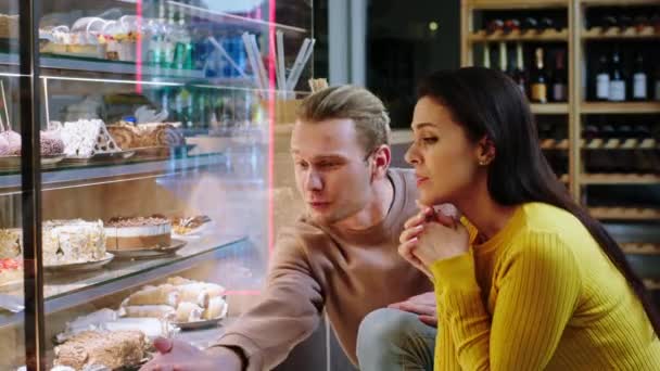 Przytulna kawiarnia podekscytowany klient mężczyzna i kobieta patrząc na lodówkę gablocie i wybierając razem ulubiony smaczny deser z lodówki gablocie — Wideo stockowe