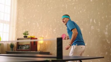 Evde pinpon oynayan karizmatik ve çekici yaşlı adam büyük bir gülümsemeyle heyecanlanıyor kırmızı raketle topları yakalıyor.