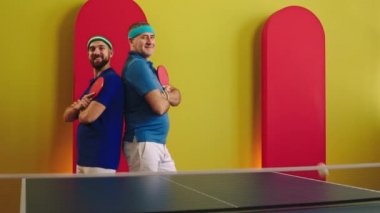 Masa tenisi maçından sonra kameranın önünde mutlu ve heyecanlı iki genç ve yaşlı adam raketi tutuyor ve dik dik bakıyorlar.