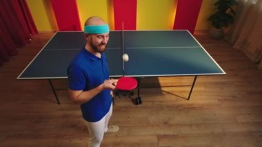 Kameranın önünde gülümseyen büyük adam pinpon oyuncusu en sevdiği raketleri kullanıyor ve topa vuruyor.