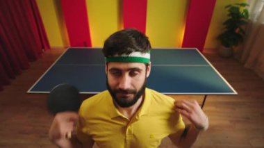 Komik masa tenisi oyuncusu doğrudan kameraya bakıyor. Oyunu başlatmaya hazırlan. Sonra masa tenisi masasına geldi ve arkadaşıyla oynamaya başladı.