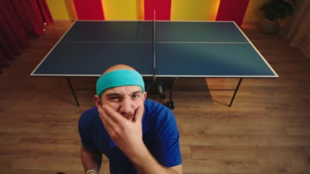 Zabawny i przystojny gracz ping ponga przygotować się do rozpoczęcia gry patrzy prosto do kamery zorganizować podbródek następnie pieszo do tenisa stołowego i zacząć grać ze swoim kolegą — Wideo stockowe