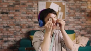 Terzi atölyesinde dans eden çekici kadın moda tasarımcısı iki düğme alır ve kulaklıklardan müzik dinlerken iş yerinde eğlenir.