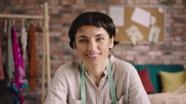 Amazing woman with a pretty smile while working at her tailoring atelier very concentrated then looking to the camera and smiling large concept of small business atelier and tailoring. Shot on ARRI — Vídeo de Stock