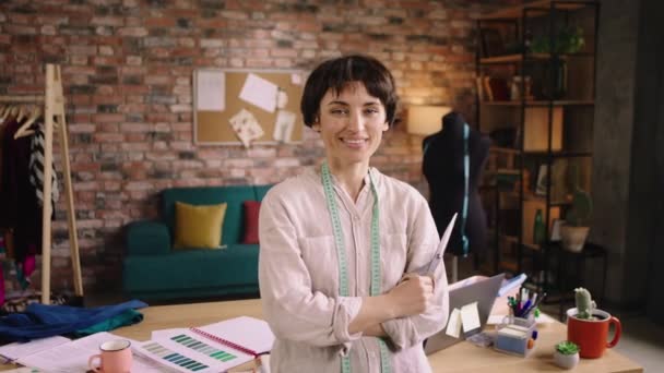 Posing in front of the camera charismatic and attractive dressmaker woman at her modern tailoring atelier she holding the tailoring scissors and smiling cute — Stockvideo