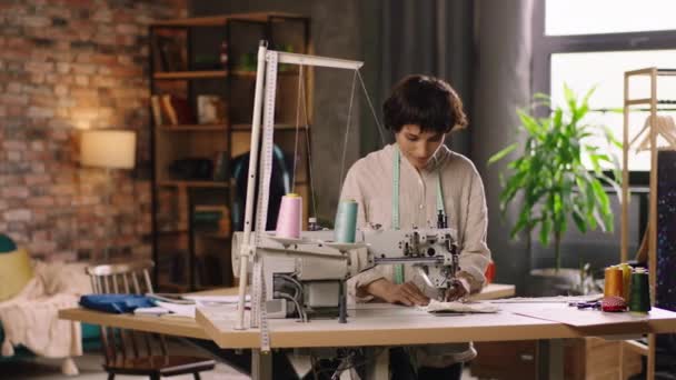 她在裁缝店里用缝纫机裁缝店里迷人的女裁缝高兴而专注地工作在新的系列上，她在相机前缝制一些面料 — 图库视频影像