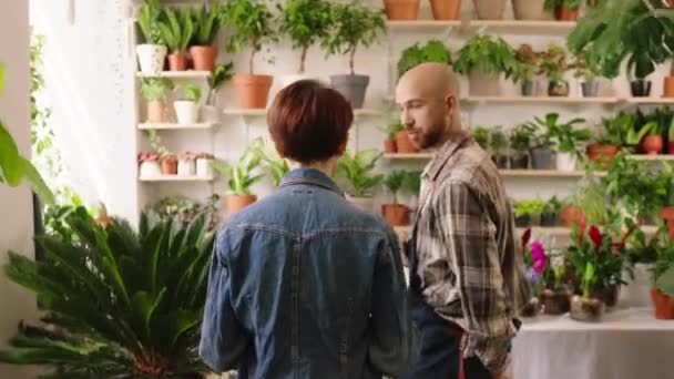 In the floral store the florist man make a excursion to the new shop assistant he explains how to take care of flowers teamwork and collaboration with happy co workers. Shot on ARRI Alexa Mini — Vídeos de Stock