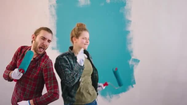 Charismatický vtipný pár dobře vypadající začít zpívat se štětcem a tancem při malování stěn v obývacím pokoji — Stock video