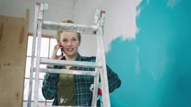 Duvarları boyarken ve terazide dururken gülümseyen güzel bir kadın bir telefon alır ve biriyle konuşur.