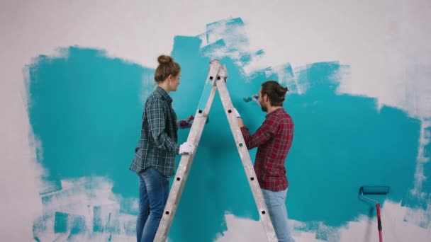 Egy pár nagyon karizmatikus festőfalat készítenek otthon a nappaliban, kék színben, ahogy a nagyméreteken állnak. — Stock videók