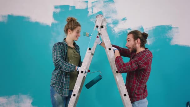 Attraente coppia caucasica mentre dipinge le pareti a casa giocando con i piccoli pennelli e sorridendo grande e in piedi sulla scala — Video Stock