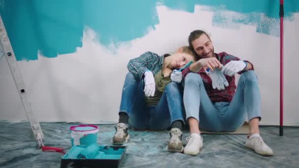 Casal carismático cansado juntos de pé ao lado da parede colorida e fazer uma pausa que pintam diante das paredes em uma cor azul — Vídeo de Stock