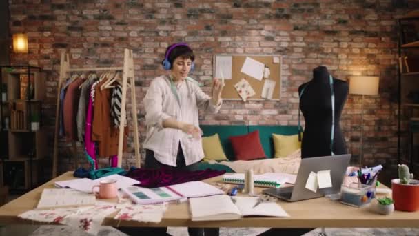 Very awesome woman talented fashion designer dancing over her workplace table she listen music from the headphones and feeling relaxed at the tailoring atelier. Shot on ARRI Alexa Mini — Vídeo de Stock