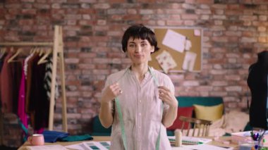 Güzel bayan terzinin terzi atölyesinde kameranın önünde mutlu poz vermesi küçük işletme terziliğinin büyük bir konseptidir.