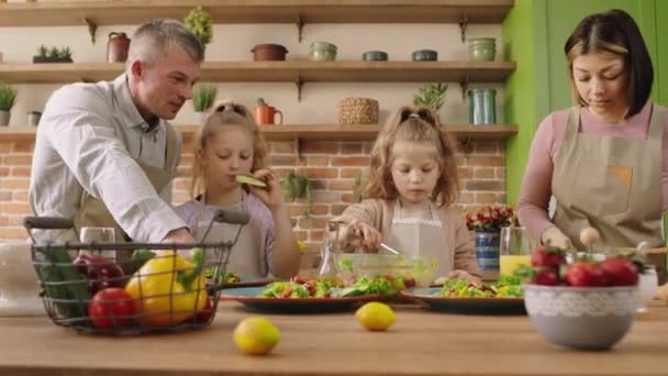 En casa en la cocina grande y luminosa feliz y bien parecido familia mamá, papá y dos hijas preparando el desayuno juntos discuten y sonríen grande — Vídeos de Stock
