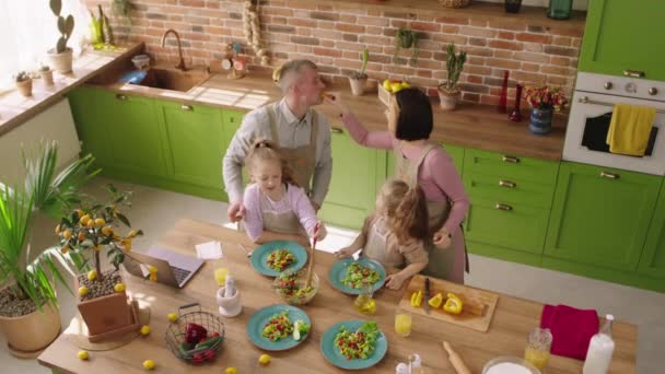 Tomando vídeo a partir do up de uma grande cozinha rústica jovem família pai mãe e duas meninas preparando um almoço saudável formar as leguminosas na ilha da cozinha — Vídeo de Stock