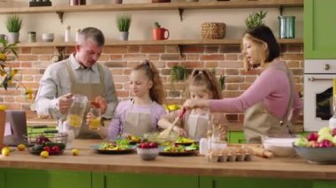 Güzel bir aile için mutlu bir sabah. Genç ebeveynler ve iki kız mutfak adasında hız yapıyorlar. Birlikte kahvaltı hazırlıyorlar.