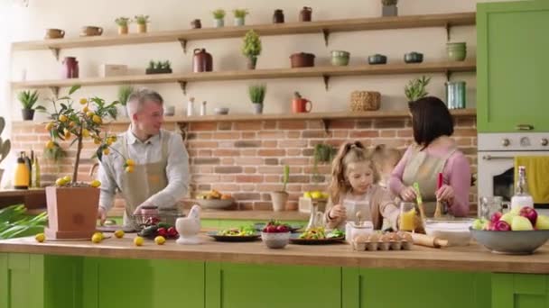 Счастливые две девочки весело провести время со своими родителями на острове кухни они готовят вместе ужин маленькая девочка помогает своей маме приготовить вкусную еду — стоковое видео