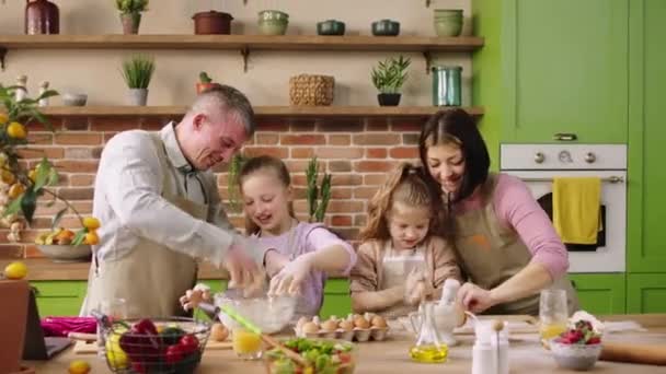 Di depan kamera, keluarga muda Kaukasia yang bahagia memasak bersama di pulau dapur dengan sangat gembira ayah mencampur adonan dengan makanan penutup yang lezat. 4k — Stok Video