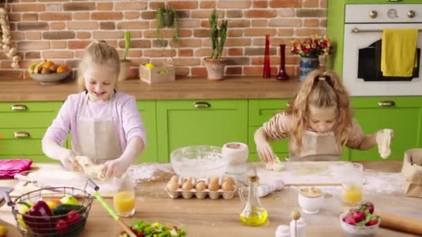 Happy lachende schattige meisjes twee zussen op het keukeneiland neem het keukenschort en het bereiden van het deeg de heerlijke koekjes ze besteden heerlijke tijd samen — Stockvideo