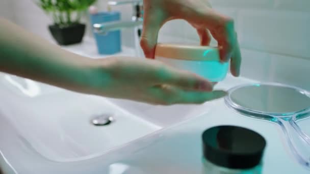 В светящейся ванной комнате, снимая видео, как женщина раскрывает увлажняющий крем для рук и массирует руки, а затем заботится о своей коже. — стоковое видео
