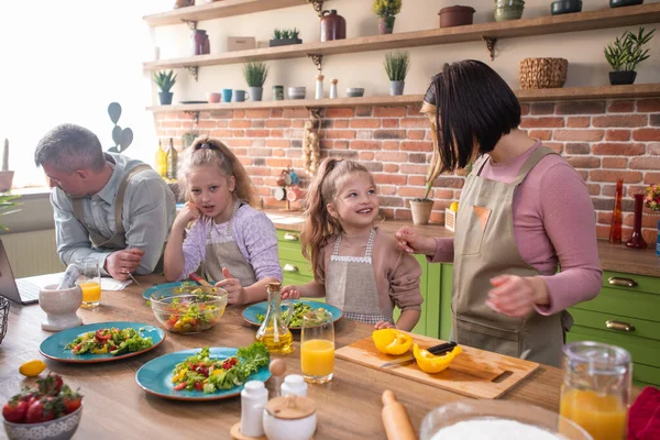 Excited Caucasian family parents and two kids girls happy playing rock paper scissors before start to cook the dinner together at the rustic kitchen island — Stock Photo, Image
