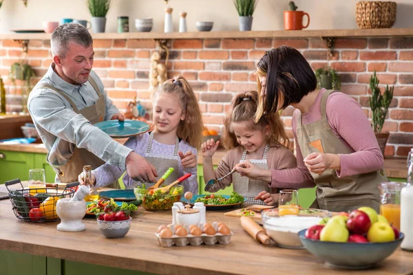 Fantastisk ser familjen på köksön förbereder lite mat tillsammans de fortkörning tid föräldrar har kul med sina barn två karismatiska döttrar — Stockfoto