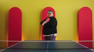 Kameranın önünde poz veren karizmatik şişman adam ping çalmaya başlamadan önce el ele tutuşup raketi tutuyor.