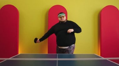 Kameranın önünde karizmatik şişman adam pinpon oynamaya hazır ol. Elinde kırmızı raketini tutuyor ve yavaşça kameraya doğru ilerliyor.
