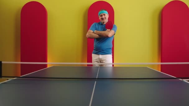 Conceito de esporte e estilo de vida saudável homem velho muito carismático com um grande sorriso posando na frente da câmera ele segurando a raquete de ping pong e cruzando as mãos — Vídeo de Stock