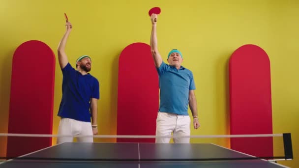 Перед камерою хороша команда з двох чоловіків танцює харизматично перед початком гри в пінг-понг вони насолоджуються концепцією здорового способу життя і спорту — стокове відео