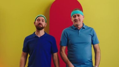 Kameranın önünde iyi görünümlü genç adam ve yaşlı adam kameranın önünde birlikte poz veriyorlar. Masa tenisi oyuncuları. Tüm ekipmanlar oyun için hazır olun.