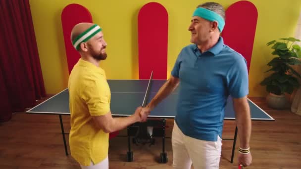 Vor der Kamera Nahaufnahme zwei Tischtennisspieler, die sich nach einem guten Spiel die Hände schütteln, dann mit verschränkten Händen in die Kamera posieren und süß lächeln — Stockvideo