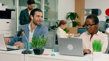 Çok büyük bir ofiste, mavi takım elbiseli çok çekici bir adam gülüyor ve yakışıklı Afrikalı iş arkadaşı arasında konuşuyor.