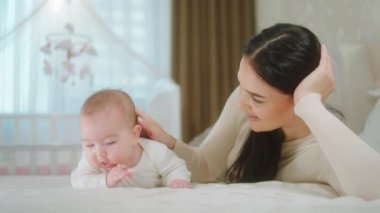 Sabahları aydınlık yatak odasında güzel anne, bebek kızıyla bebek bakıcılığı ve doğum konsepti üzerine güzel bir oyun oynuyor.