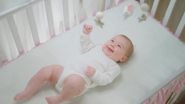 Cute little baby girl in her baby cot playing alone while looking up to the cot toys concept of childhood and health — стоковое видео