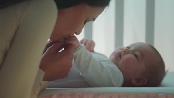 Στο υπνοδωμάτιο έννοια του μωρού και της νοσηλευτικής φροντίδας closeup στην κάμερα όμορφη μητέρα φιλιά χαριτωμένα χέρια της κόρης κοριτσάκι της, ενώ αυτή είναι ξαπλωμένη στο κρεβατάκι του μωρού — Αρχείο Βίντεο