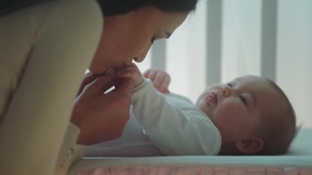 Nel concetto di camera da letto del bambino e cura infermieristica primo piano per la fotocamera bella madre baciare le mani carine di sua figlia bambina mentre lei è sdraiata sulla culla — Video Stock