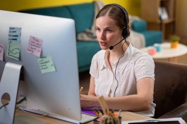 Amazing looking woman working at home customer support service she wear wireless headset and discussing through the computer