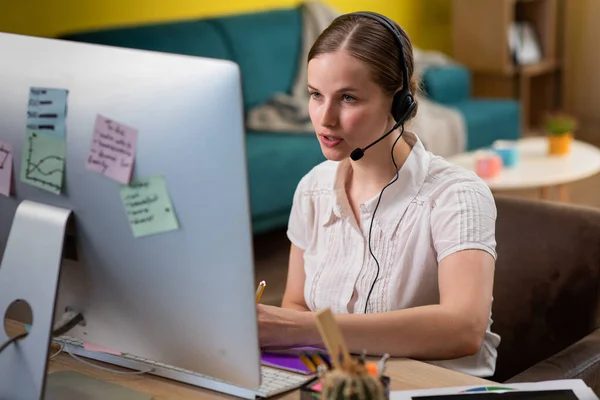 Amazing looking woman working at home customer support service she wear wireless headset and discussing through the computer — Zdjęcie stockowe