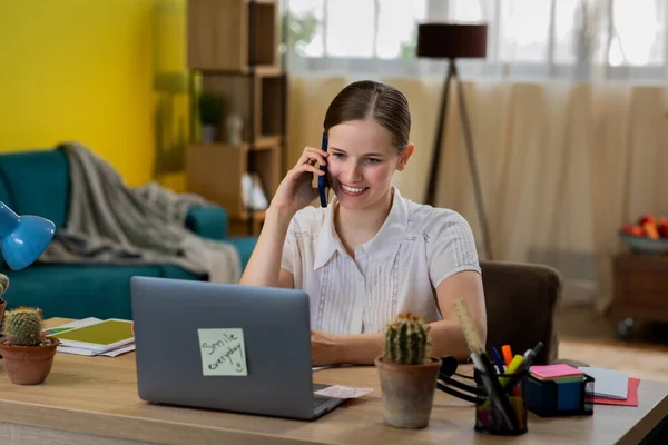 Call centre agent working from home at her laptop she make a call with a client she using the smartphone — Stockfoto