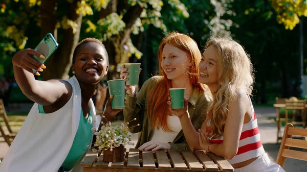 Fröhliche und aufgeregte Damengruppe in der Konditorei mitten im Park macht ein paar Selfies mit dem Smartphone — Stockfoto