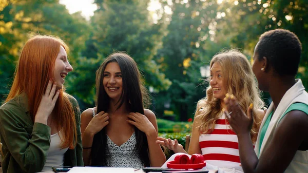 Cztery zadziwiająco piękne kobiety siedzą przy stoliku na zewnątrz w malowniczym parku, rozmawiając ze sobą i będąc radosnymi. — Zdjęcie stockowe